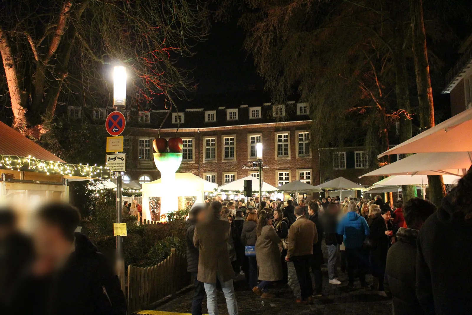X-MS-Weihnachtsmarkt am Harsewinkelplatz in Münster an der Skulptur Kirschensäule von Thomas Schütte, mit Buden und Besuchern.